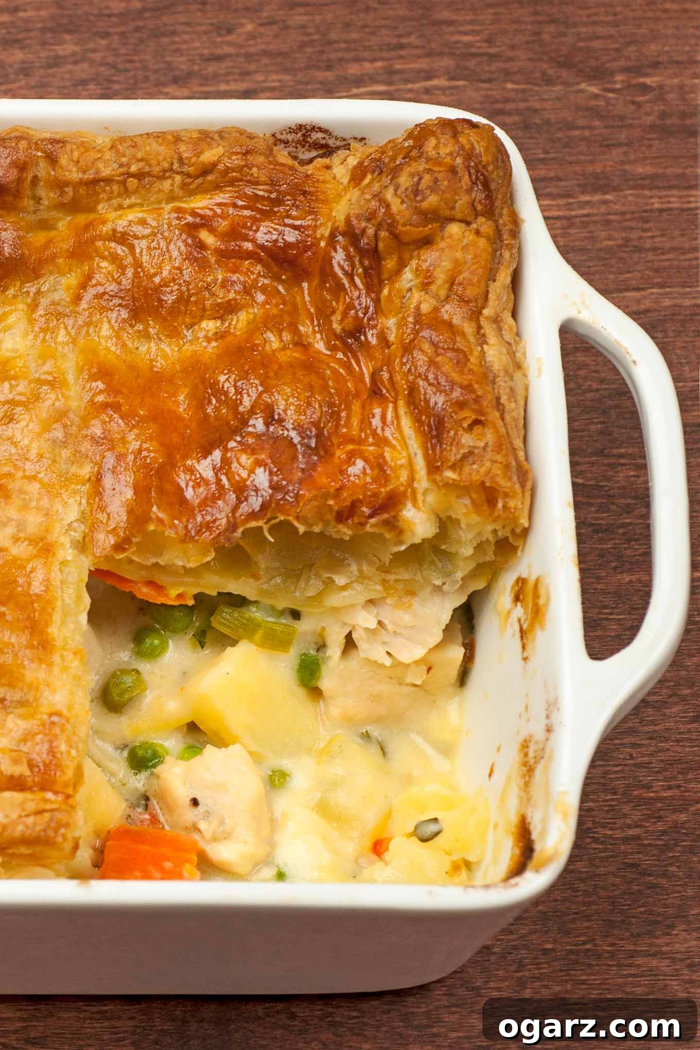 Golden-crusted chicken pot pie with a portion removed, revealing flaky pastry layers and creamy chicken filling.