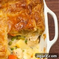 Pot pie baking dish with a single serving removed showing layers of flaky pastry and creamy chicken filling.