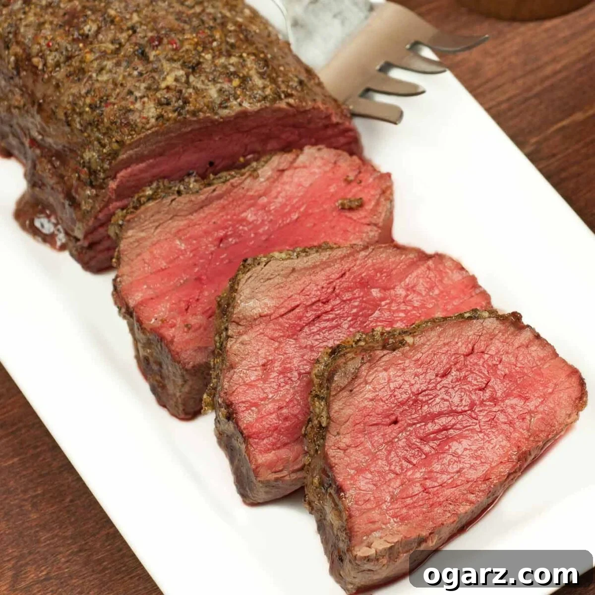 Partially carved roasted beef tenderloin on a white plate with a serving fork.