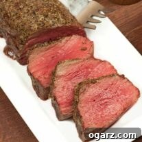 Partially carved roasted beef tenderloin on a white plate with a serving fork.