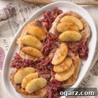 An overhead view of boneless pork chops with apple slices and caramelized red onions arranged on top - a printed tea towel and serving tongs in the background.