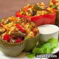 Colorful bell peppers stuffed with chopped peppers, chorizo, rice, and herbs, served on a white plate with a side of creamy dipping sauce and fresh cilantro garnish.