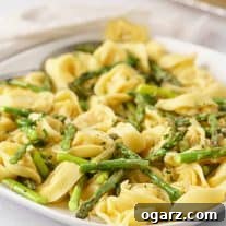 A serving plate filled with delicate cheese tortellini tossed with roasted asparagus, lemon zest, parsley, and a light cream sauce.