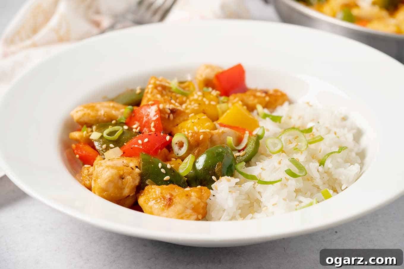 A close-up view of a hearty bowl of sweet and sour chicken, showcasing tender chicken pieces, vibrant sweet bell peppers, juicy pineapple chunks, and fluffy rice, all garnished with fresh scallions and toasted sesame seeds.