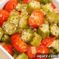 A square, white serving bowl with chunks of okra and halved cherry tomatoes sautéed with onion and garlic in olive and butter.