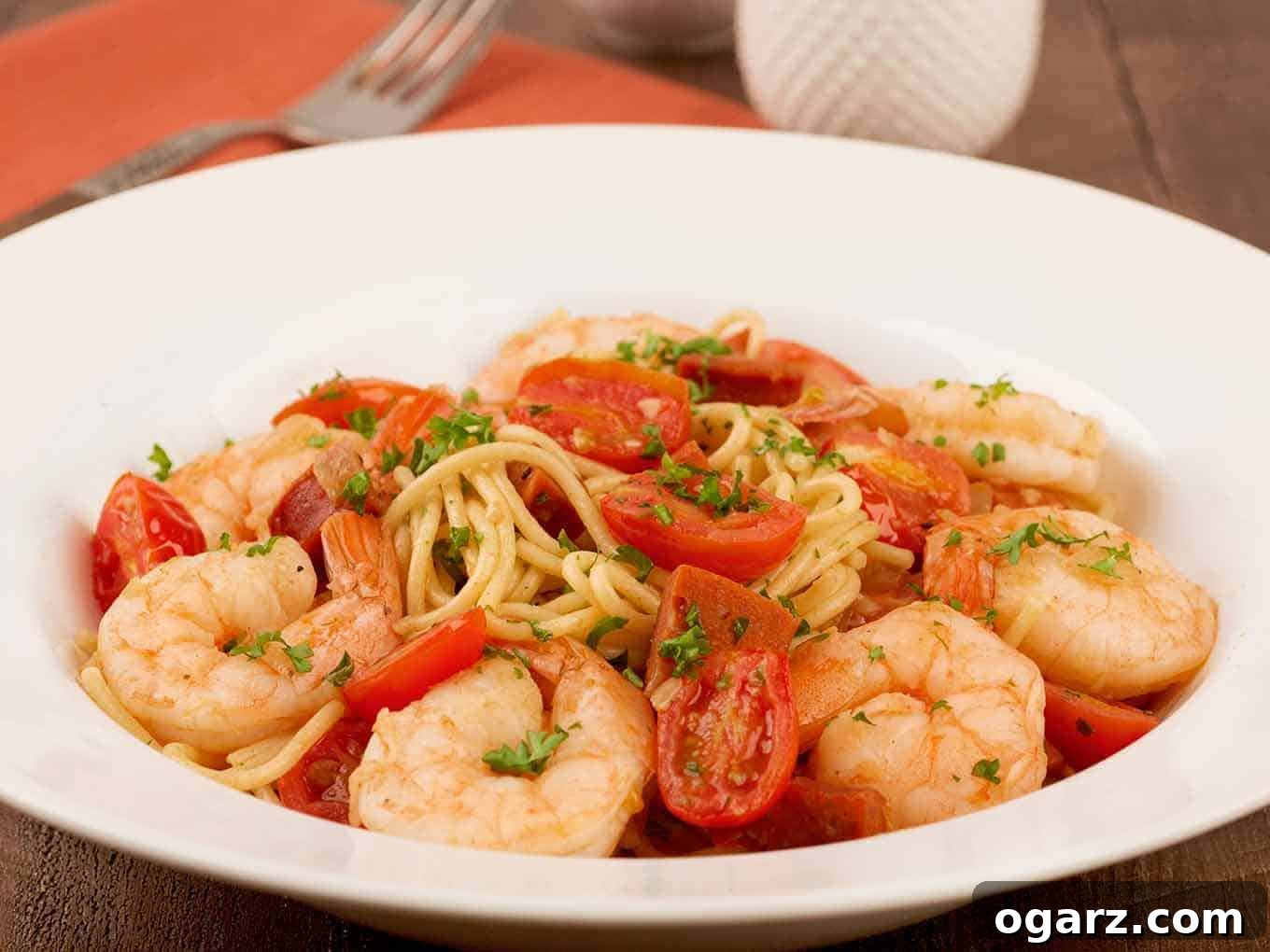 A closeup view of Spanish-style spaghetti with chorizo, garlic, onion, shrimp simmered in sherry, grape tomatoes, and parsley garnish.