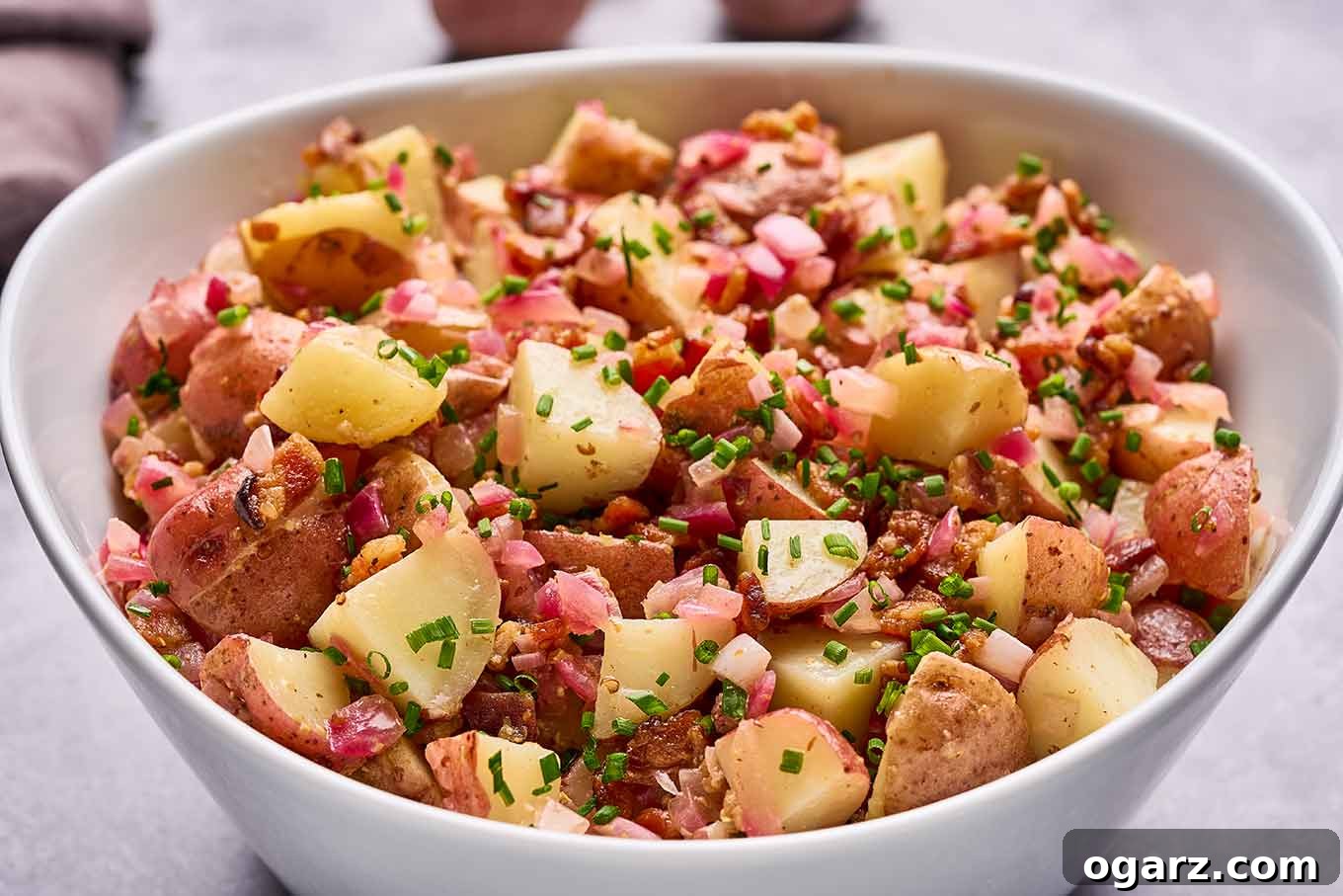 Authentic Warm German Potato Salad 6 A bowl of German potato salad made with chunks of baby red-skinned potatoes, bacon bits, red onion, chives, and warm bacon dressing.