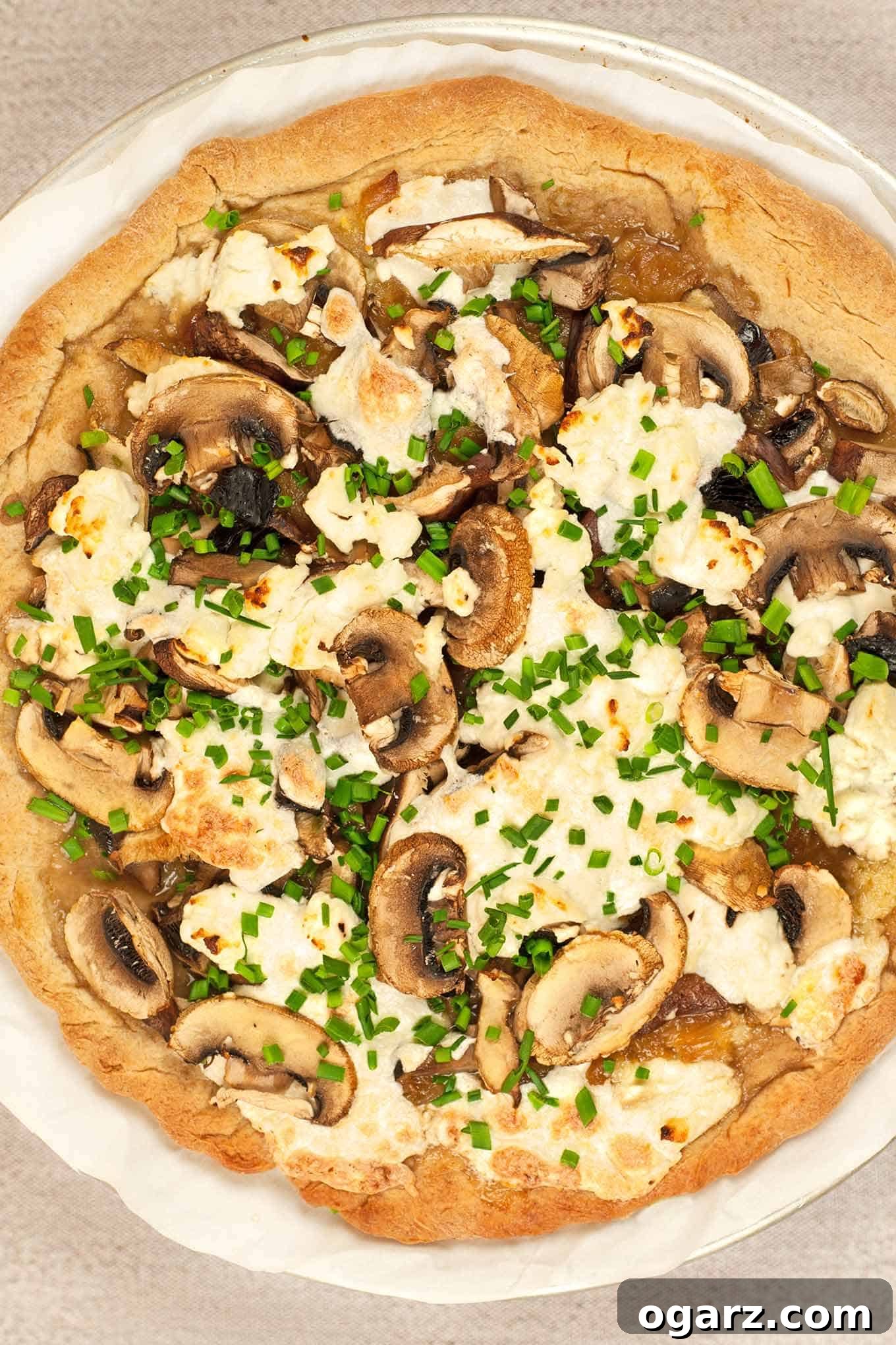 Wild Mushroom & Chèvre Pizza 2 Top view of uncut, baked pizza topped with sautéed mushrooms, caramelized onions, goat cheese, mozzarella and chives.