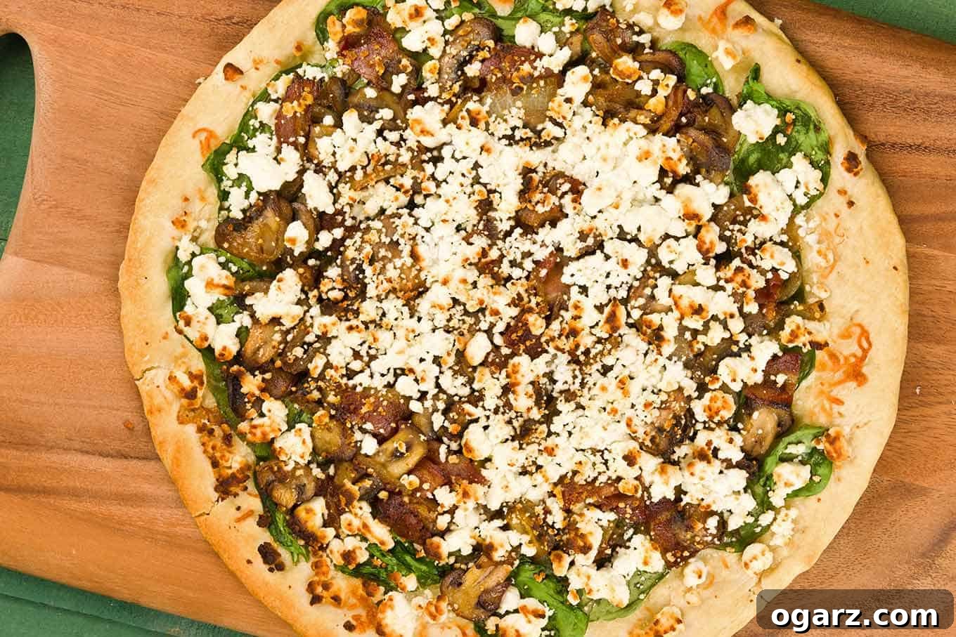 Wild Mushroom & Chèvre Pizza 3 Top view of an uncut pizza topped with spinach, mushrooms, goat cheese, and mozzarella.