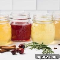 Four glass mason jars filled with homemade holiday simple syrups orange, cranberry, rosemary, and ginger, ingredients scattered in front.