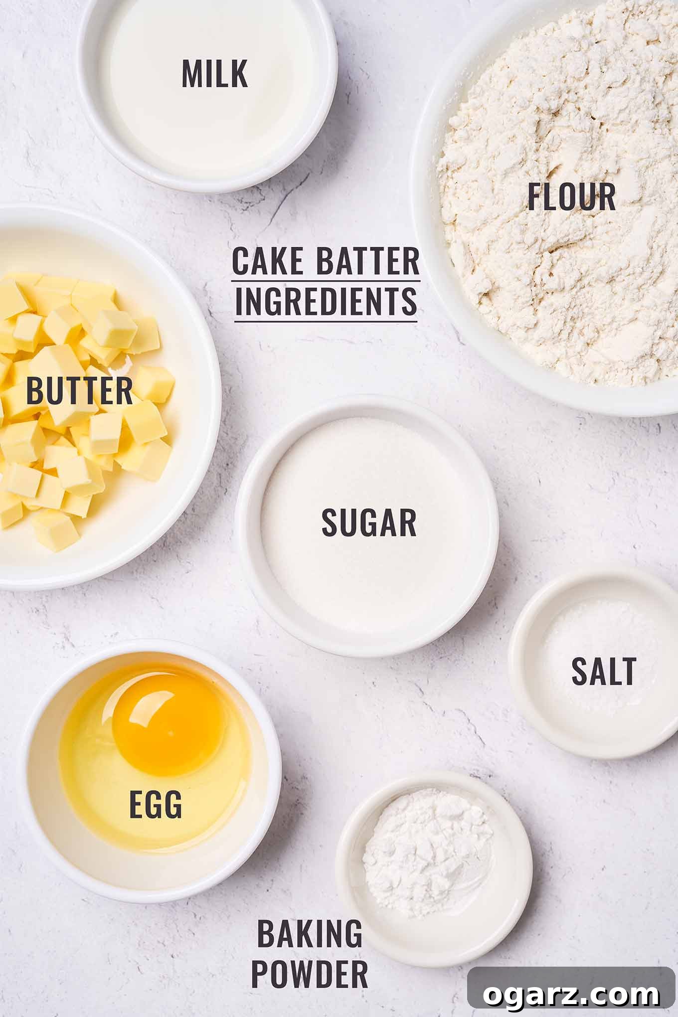 Labeled, overhead view of the ingredients for Golden Delicious apple cake batter in prep bowls; including flour, butter, sugar, egg, milk,baking powder, and salt.