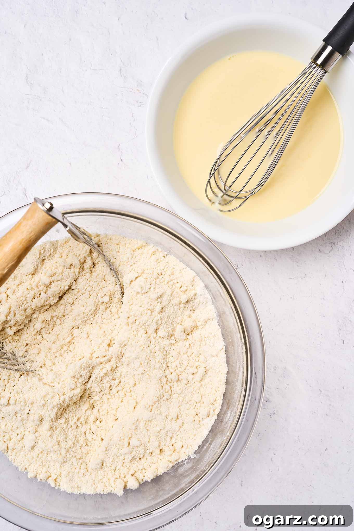 Making Golden Delicious apple cake; two mixing bowls, one with dry ingredients showing consistency, another bowl with wet ingredients and a whisk.