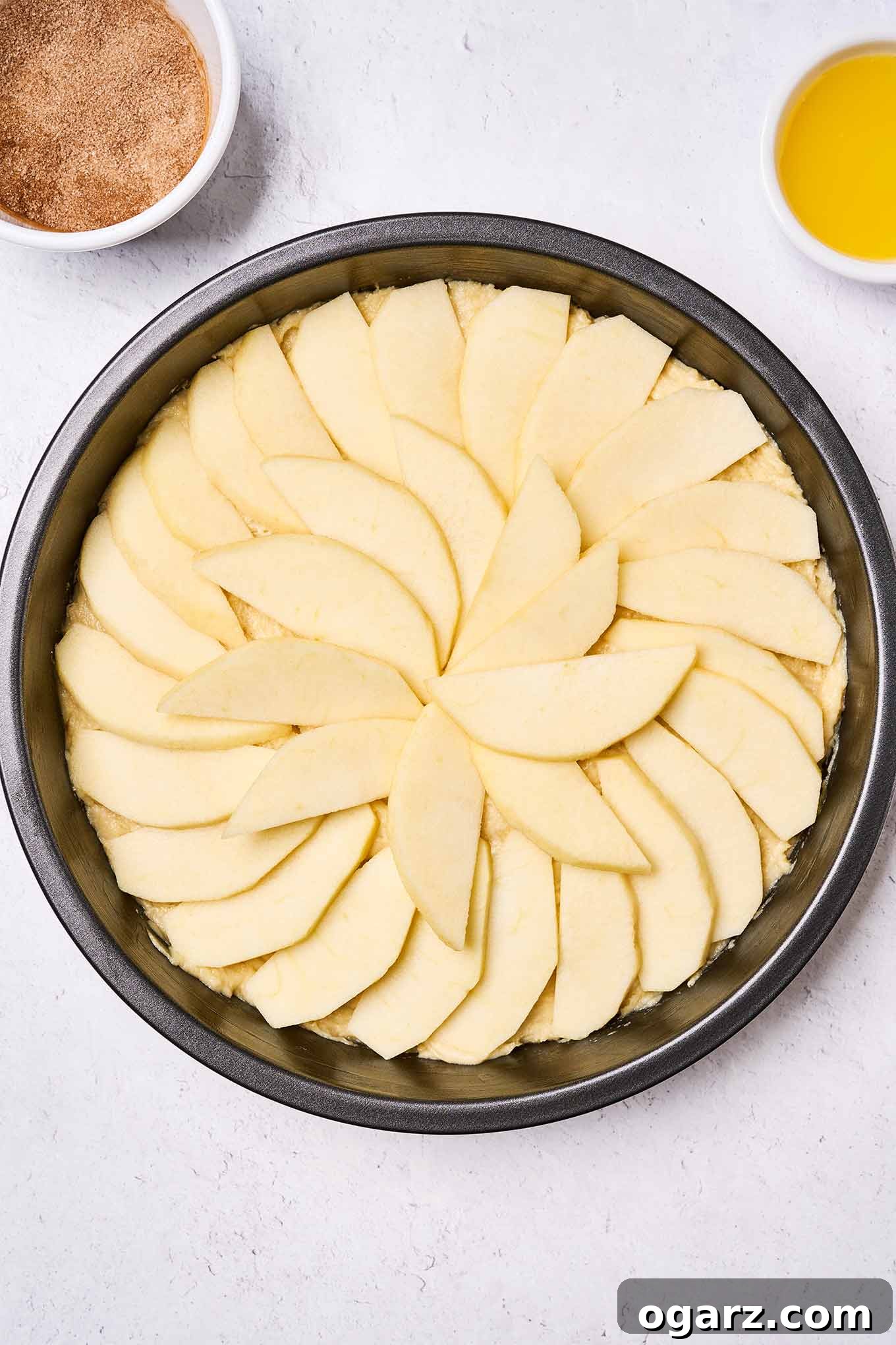 Golden Delicious apple cake batter in the pan and topped with apple slices, waiting to be topped with melted butter and cinnamon sugar.