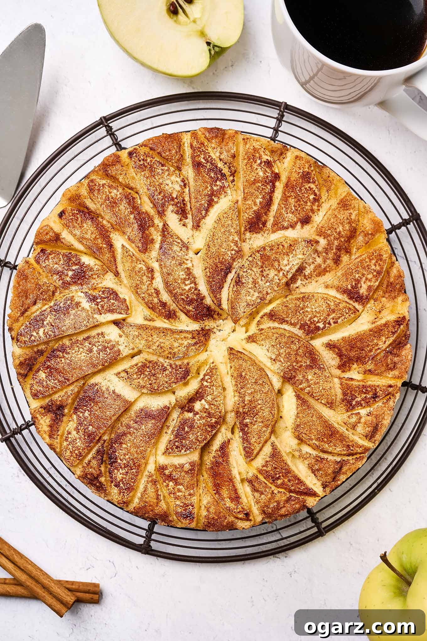 Freshly baked apple cake topped with sliced Golden Delicious apples and cinnamon sugar, cooling on a wire rack, waiting to be sliced.