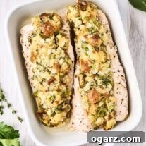 Two stuffed turkey tenderloins in a white oblong baking dish surrounded by fresh parsley, sage and thyme.