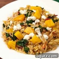 A plate of orzo pasta mixed with roasted golden beets, sautéed greens, and topped with crumbled goat cheese.