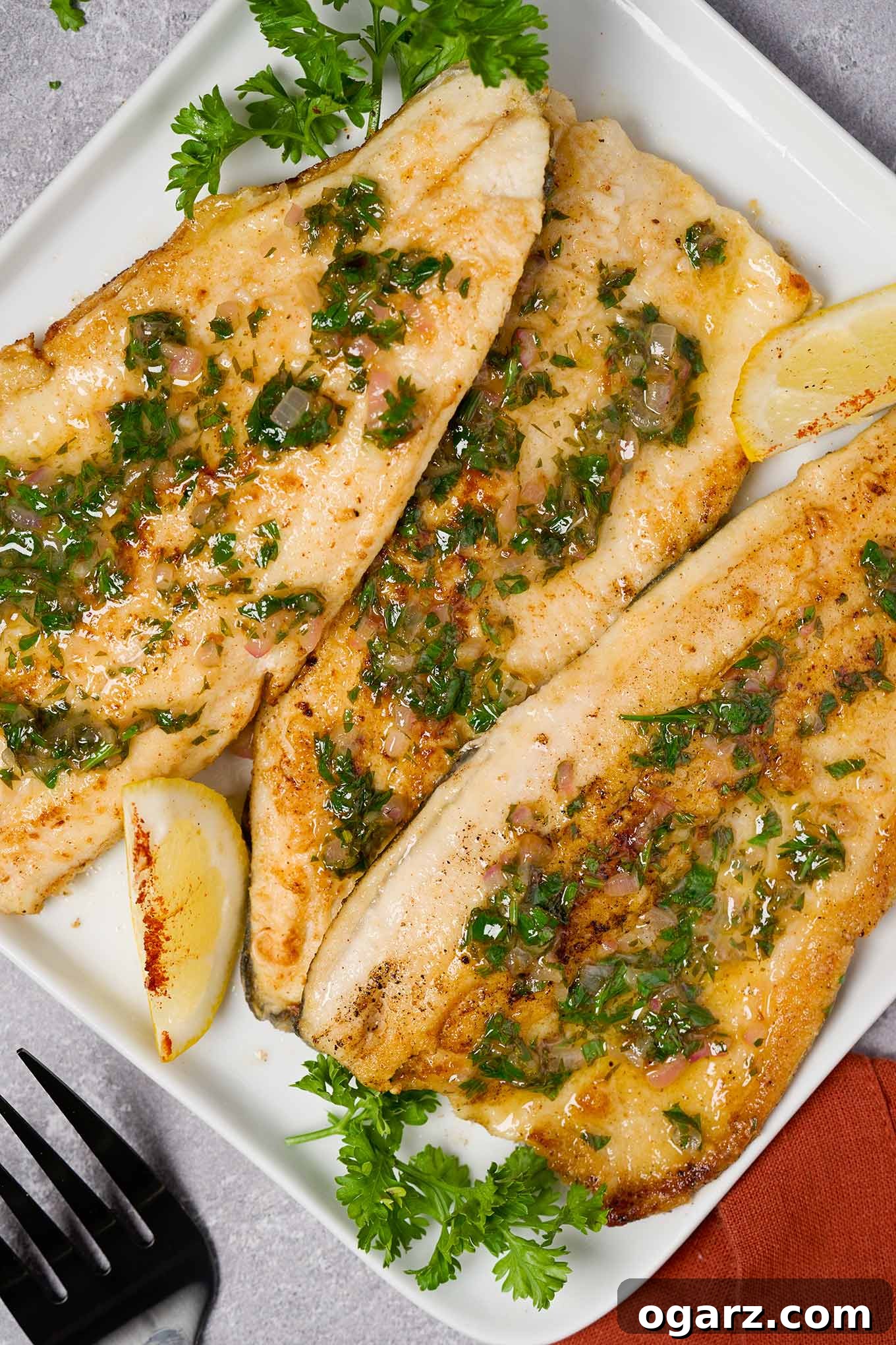 A serving plate of trout meunière topped with lemon, parsley, and minced shallot butter, garnished with lemon wedges and parsley.