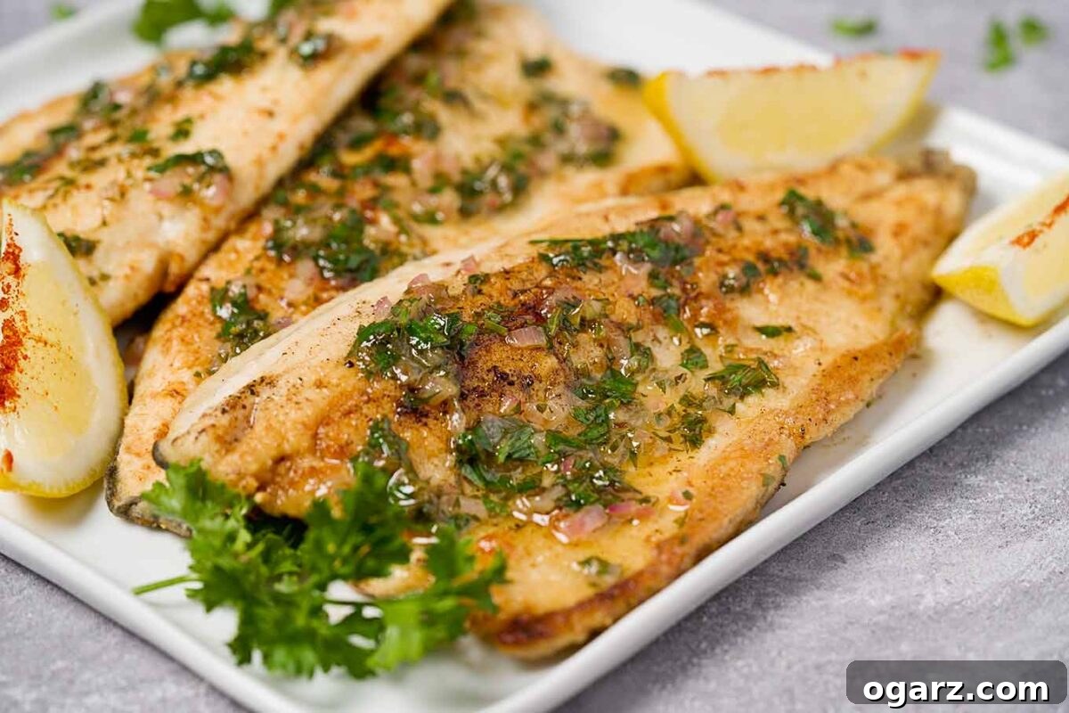 A close up of rainbow trout meunière showing a drizzle of lemon-parsley butter. Lemon wedges and sprigs of parsley garnish the plate.