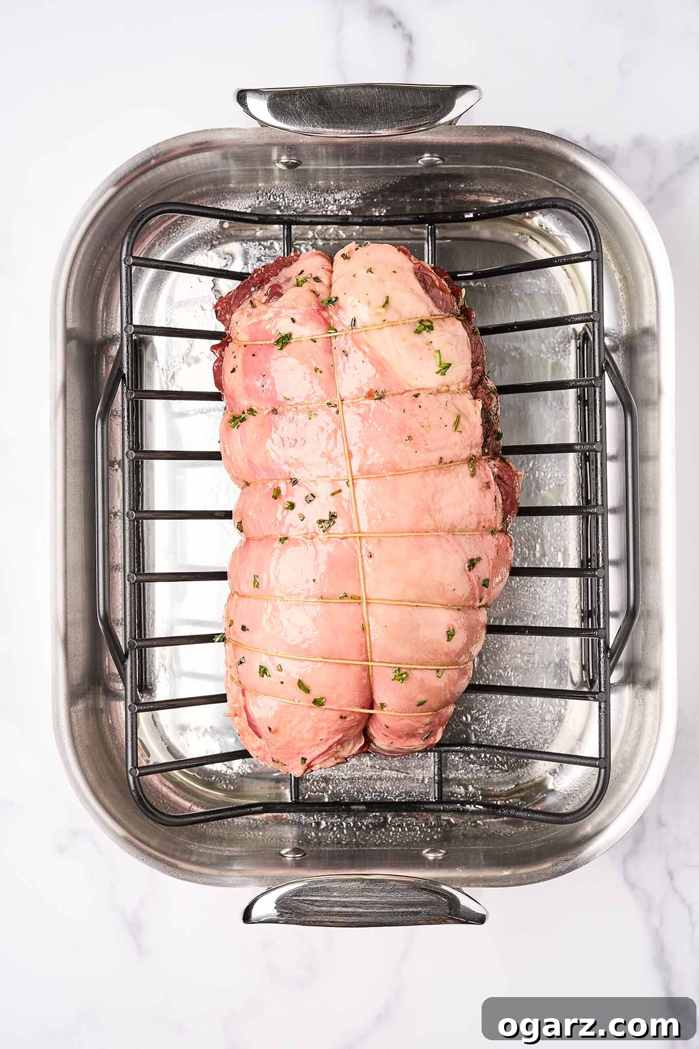 Succulent Roasted Boneless Lamb Leg 6 An overhead view of a boneless leg of lamb in a roasting pan ready for the oven, showing the proper way to tie it with kitchen twine.