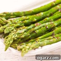 Steamed asparagus spears tossed in brown butter and balsamic vinegar on a white serving plate.