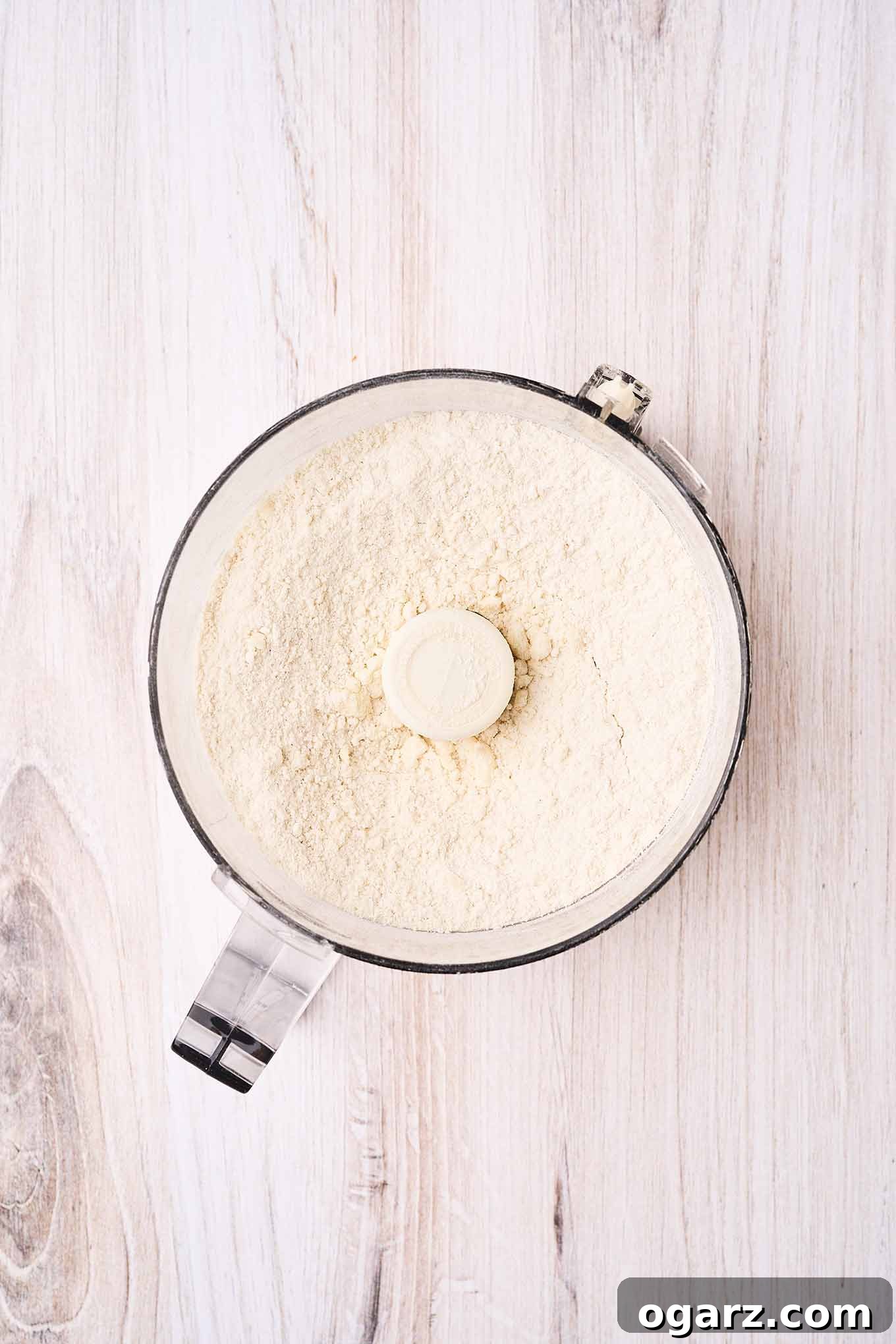 An overhead view of pie crust ingredients, pulsed together in the work bowl of a food processor.