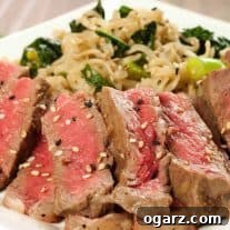 Sliced mirin-marinated strip steak topped with sesame seeds, served alongside scallion and kale ramen noodles on a white plate.