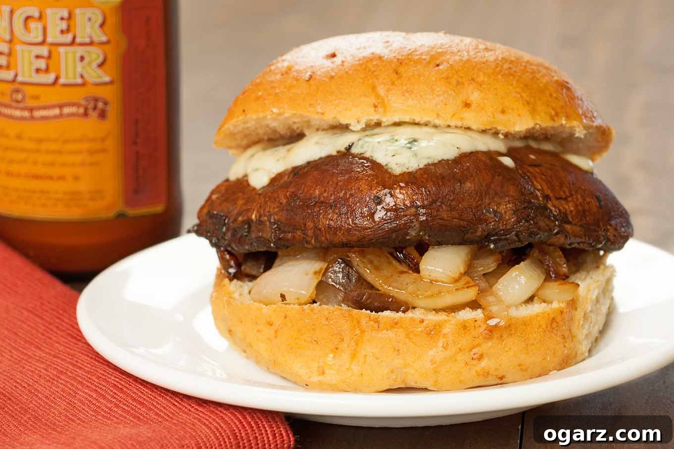 Sticky Balsamic Portobello Burgers 3 A perfectly grilled balsamic-glazed portobello mushroom burger nestled in a soft hamburger bun, topped with generously sautéed onions and a creamy, melted layer of Gorgonzola cheese. A delightful side view showcasing the layers of flavor.