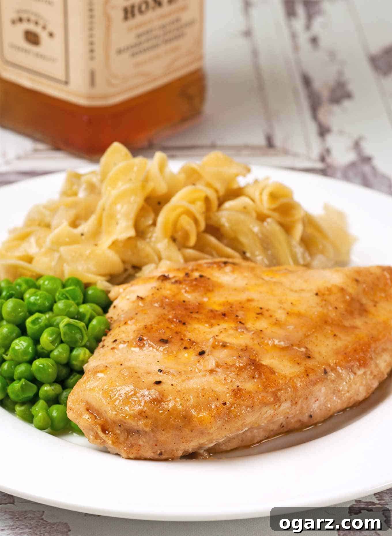 Golden Honey Whiskey Chicken 2 Whiskey glazed chicken breast served with buttered egg noodles and green peas on a white plate.
