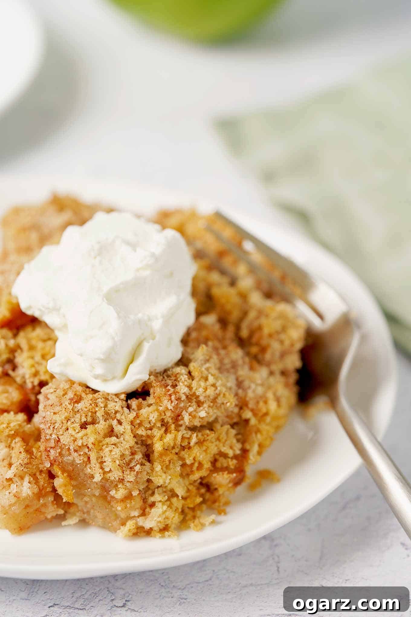 Golden Spiced Apple Bake 7 Close-up photo of a generous slice of Apple Brown Betty on a white plate, topped with a dollop of fresh whipped cream, showcasing its golden brown, textured topping.
