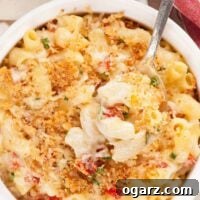 A spoonful of creamy goat cheese and sun-dried tomato macaroni and cheese, topped with crispy golden crumbs being lifted from a round white casserole.