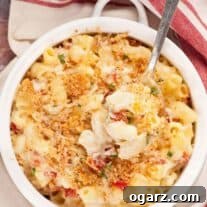 A spoonful of creamy goat cheese and sun-dried tomato macaroni and cheese, topped with crispy golden crumbs being lifted from a round white casserole.
