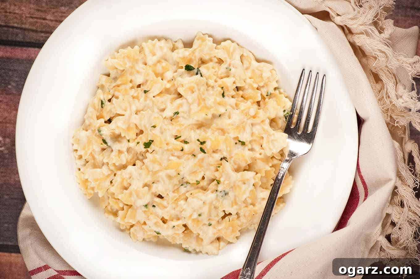 Luxurious Stovetop Mac and Cheese 2 White bowl filled with creamy stovetop macaroni and cheese made with bowtie pasta, garnished with parsley, and served with a fork.