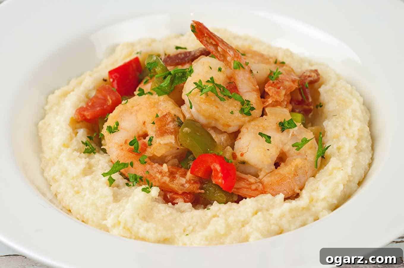 Coastal Comfort Shrimp and Grits 3 A white bowl of sautéed shrimp, bell peppers, and bacon served over creamy, cheesy grits and garnished with fresh parsley.
