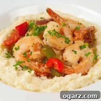 A white bowl of sautéed shrimp, bell peppers, and bacon served over creamy, cheesy grits and garnished with fresh parsley.