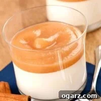 A single serving of elegant panna cotta topped with cinnamon-spiced pear puree in a clear glass, presented as a perfect fall dessert.