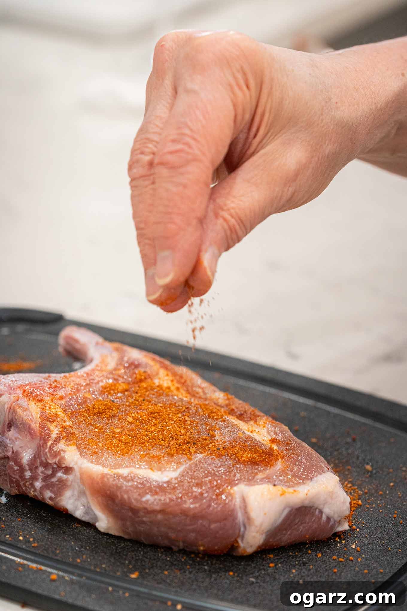 Effortless Grill Master Rub 4 BBQ spice rub being sprinkled onto pork chops showing how to get even distribution of the rub on meat.