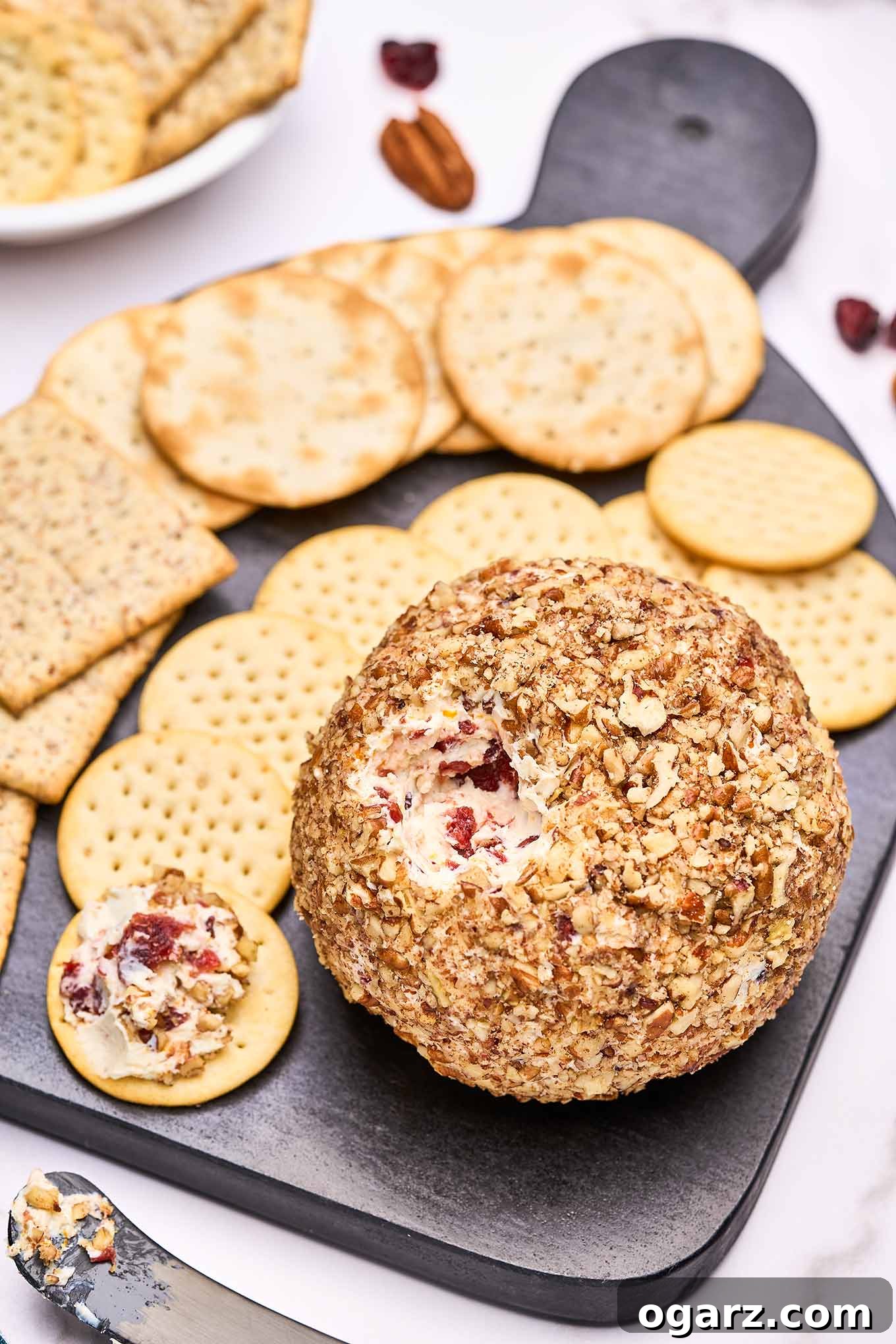 A close up view of a festive cranberry cheese ball with a portion removed, revealing a creamy interior studded with dried cranberries and fresh orange zest, ready to be served.