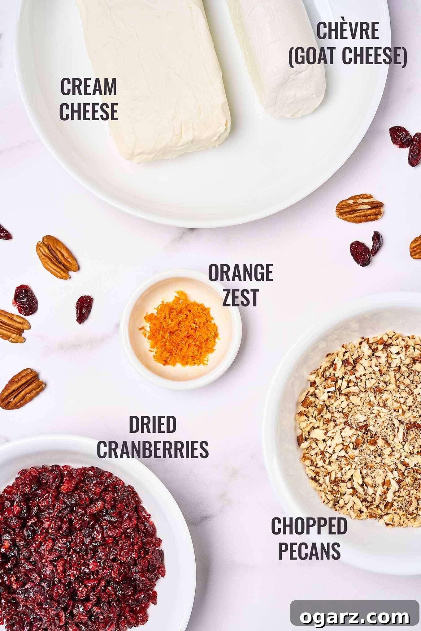 A labeled overhead view showing all the essential ingredients for a cranberry cheese ball, including cream cheese, goat cheese, orange zest, dried cranberries, and toasted pecans arranged neatly.
