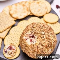 A close up view of a cranberry cheese ball with a portion removed revealing the creamy cheese studded with dried cranberries and fresh orange zest.