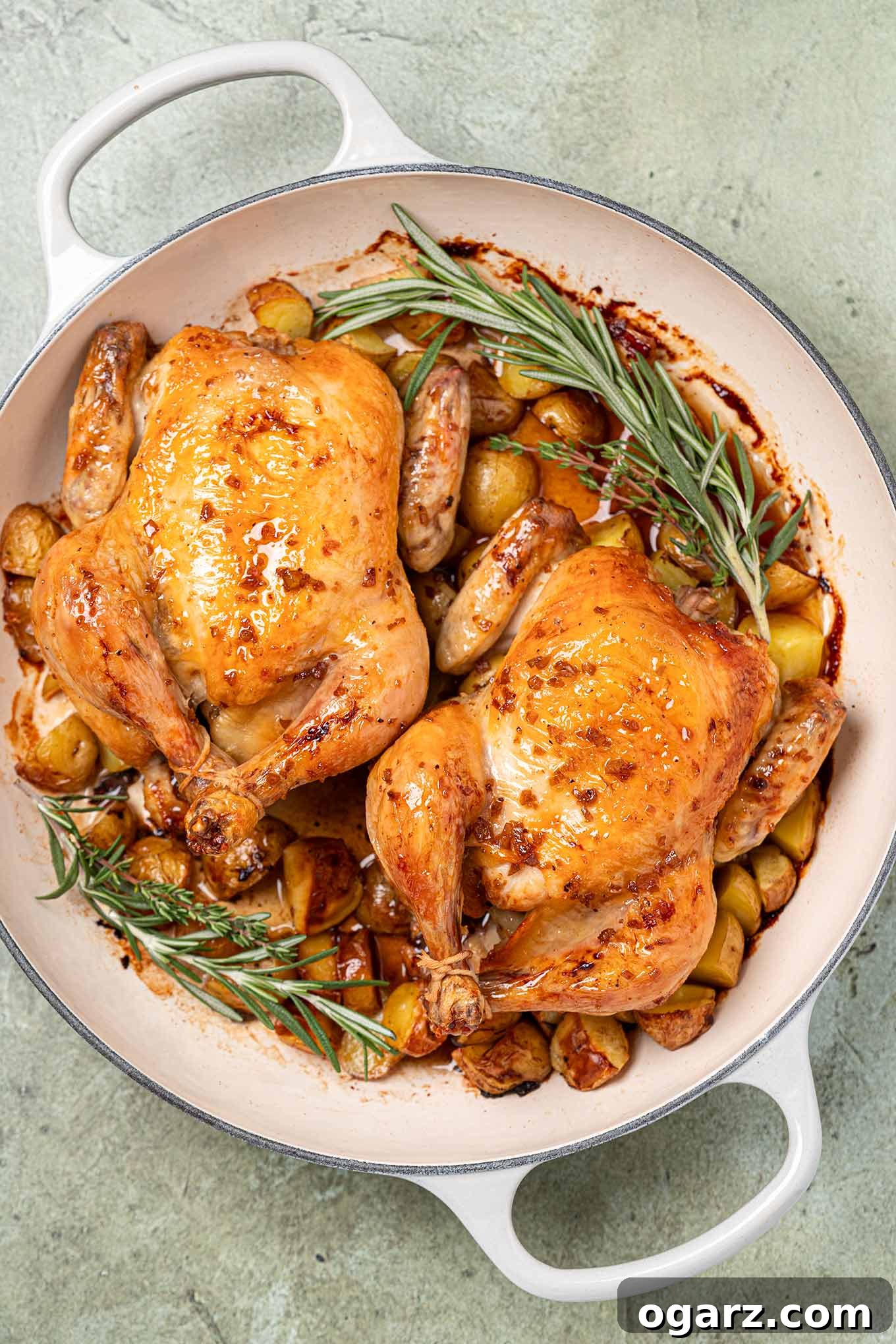 Two roasted cornish hens glazed with bourbon and honey in an enameled cast iron pan with baby potatoes and a garnish of fresh rosemary and thyme.