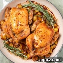 Two roasted cornish hens glazed with bourbon and honey in an enameled cast iron pan with baby potatoes and a garnish of fresh rosemary and thyme.