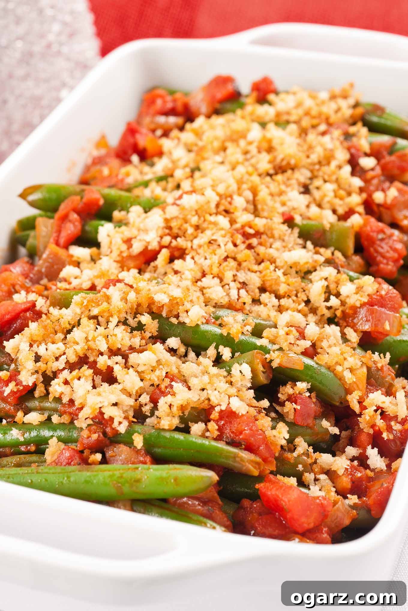 A vibrant Italian-inspired green bean casserole, topped with golden toasted bread crumbs and grated Parmesan cheese, nestled in a white oblong baking dish. Fresh tomatoes add a splash of color to this wholesome side.