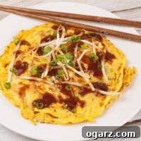 Golden Egg Foo Young omelet topped with brown gravy, bean sprouts, and sliced green onions on a white plate with chopsticks.