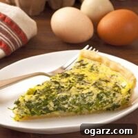 A slice of spinach and cheese quiche on a plate with a fork, fresh eggs and and a tea towel in the background.