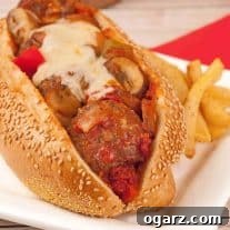 Toasted sesame seed sub roll filled with savory meatballs, rich marinara sauce with sautéed mushrooms and bell peppers, and melted mozzarella cheese, served alongside seasoned French fries.