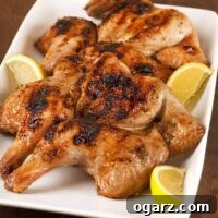 Grilled spatchcocked, honey-glazed Cornish hens with charred skin on a white platter with lemon wedges on the side.