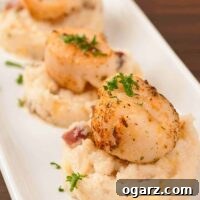 Close-up of golden-brown seared scallops resting on a bed of rich, creamy bacon grits with specks of green parsley.