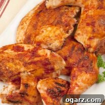 A white serving platter with bbq chicken parts, leg quarters, breasts, and wings. A sprig of parsley on the side and a jar of bbq spice rub in the background.