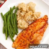 Southern Creole Catfish Bake 3 Baked Creole catfish fillet served with roasted cauliflower and steamed green beans on a white plate.