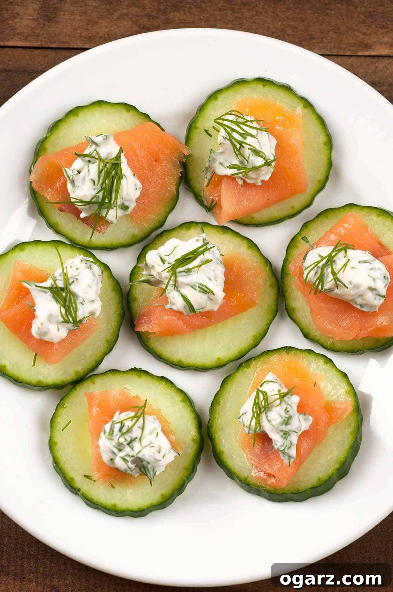 A beautifully arranged serving platter of Smoked Salmon Cucumber Bites, featuring crisp cucumber slices topped with thin rolls of smoked salmon, dollops of creamy dill and lemon cream cheese, and fresh dill garnish.